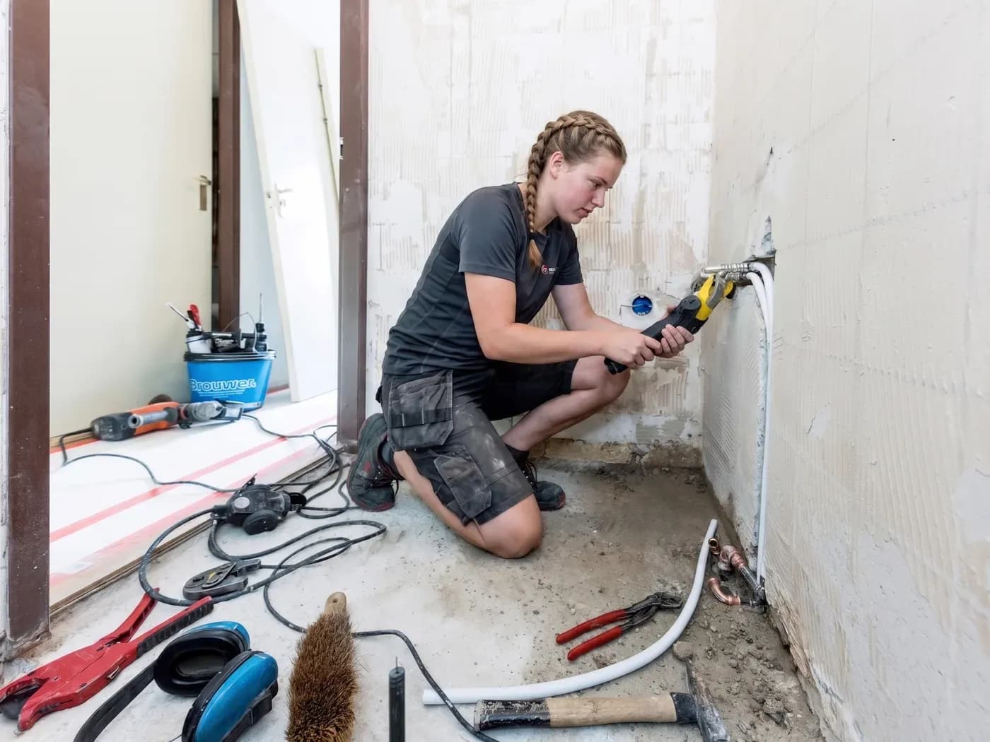 Monteur die leidingwerk aansluit in een badkamer in aanbouw, met gereedschap op de vloer